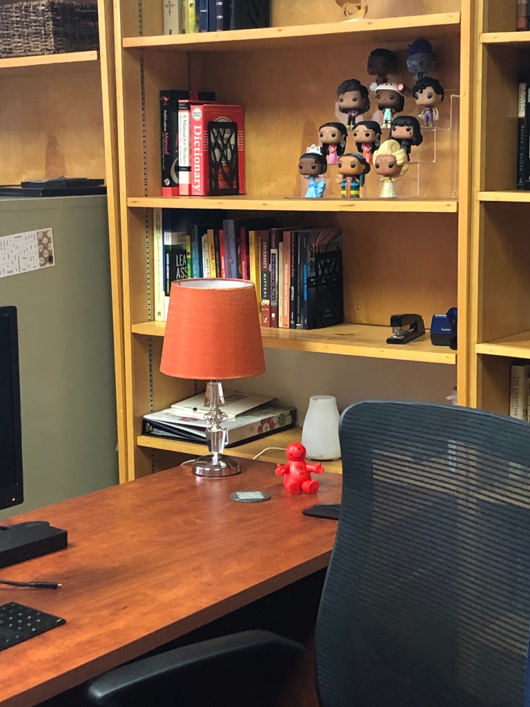 Partial photo of desk with orange lamp in front of bookshelves featuring a display of Funko Pop characters.